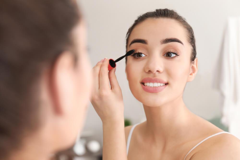 Woman applying mascara in front of mirror
