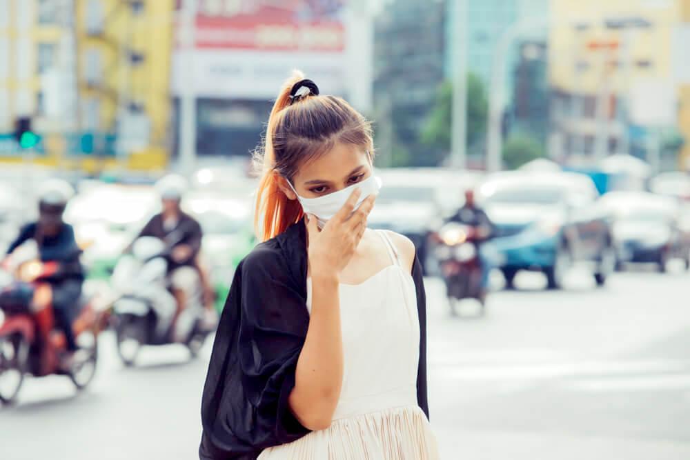 Woman covering her face with a face mask, city pollution concept