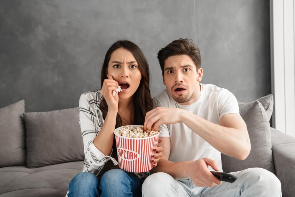 Couple watching TV at home while eating popcorn