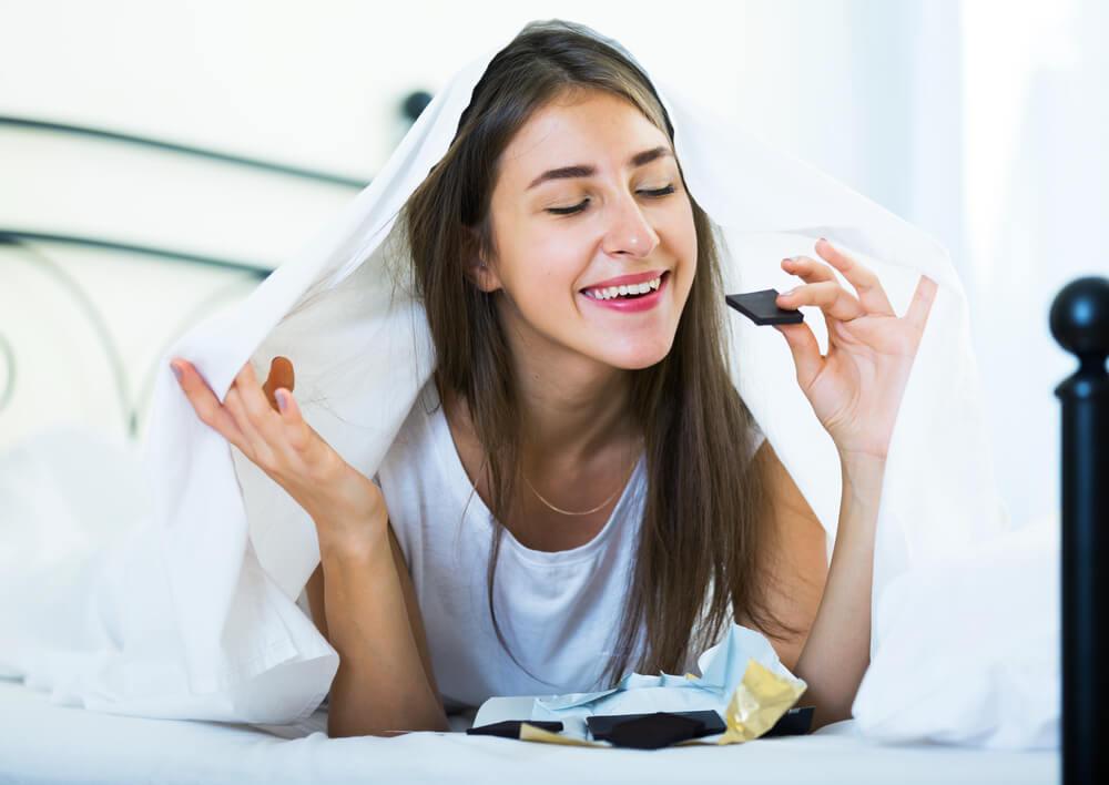 Woman eating dark chocolate in bed