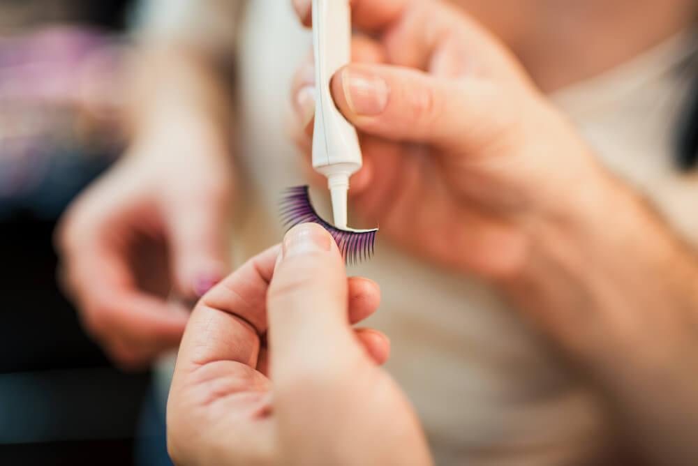 Hand putting glue on false lash strip