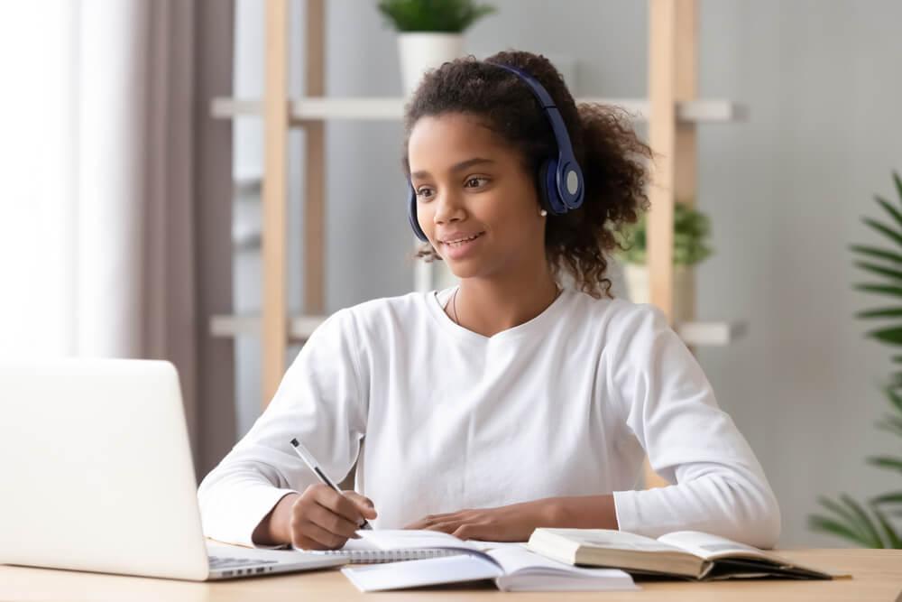 Woman with headphones looking at laptop and taking notes