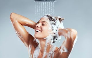 Woman shampooing hair in shower with shampoo running onto skin